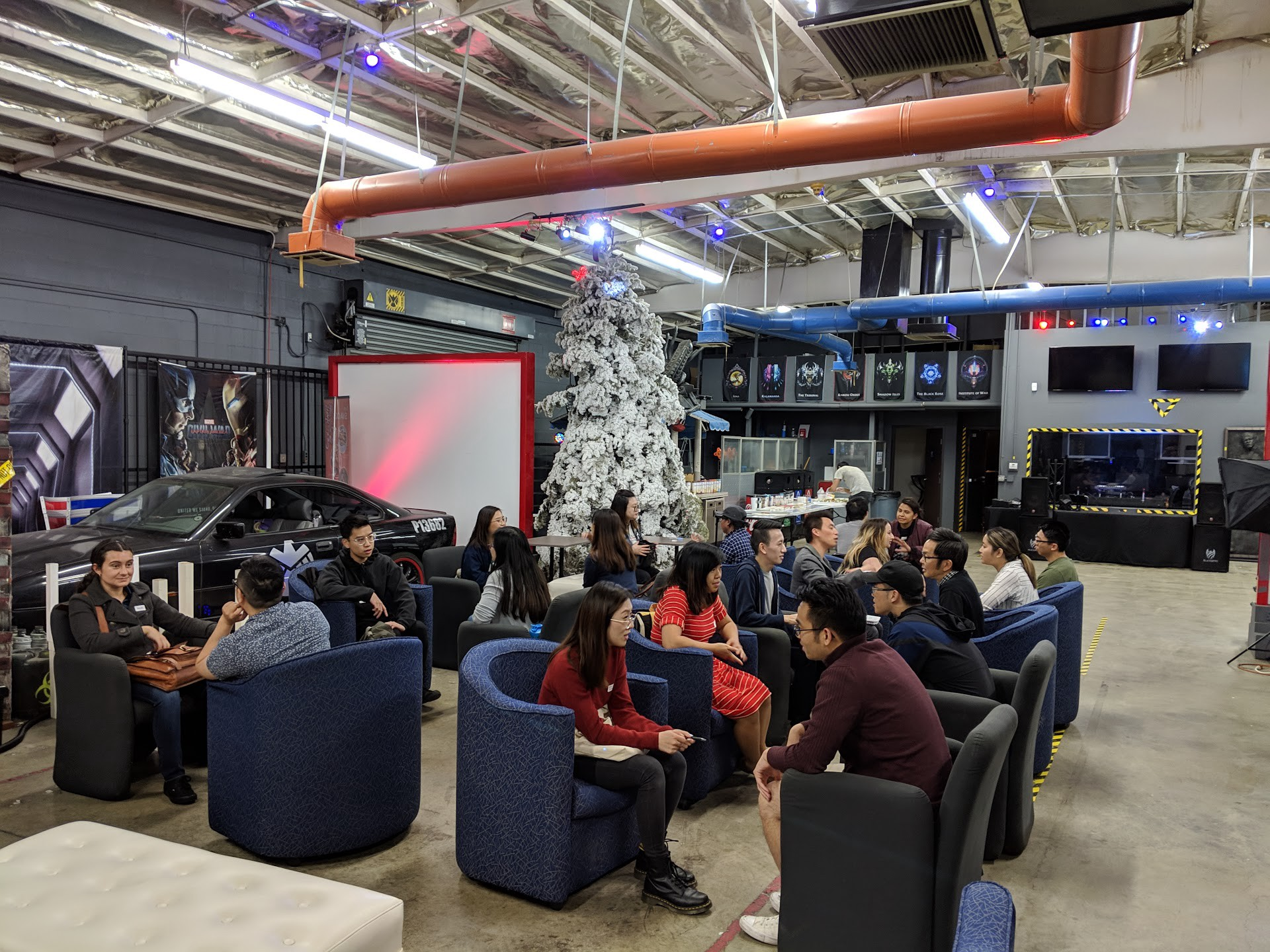 Warehouse with white Christmas tree prop and a fake police car in the background. Sets of 2 chairs set up with people facing each other.