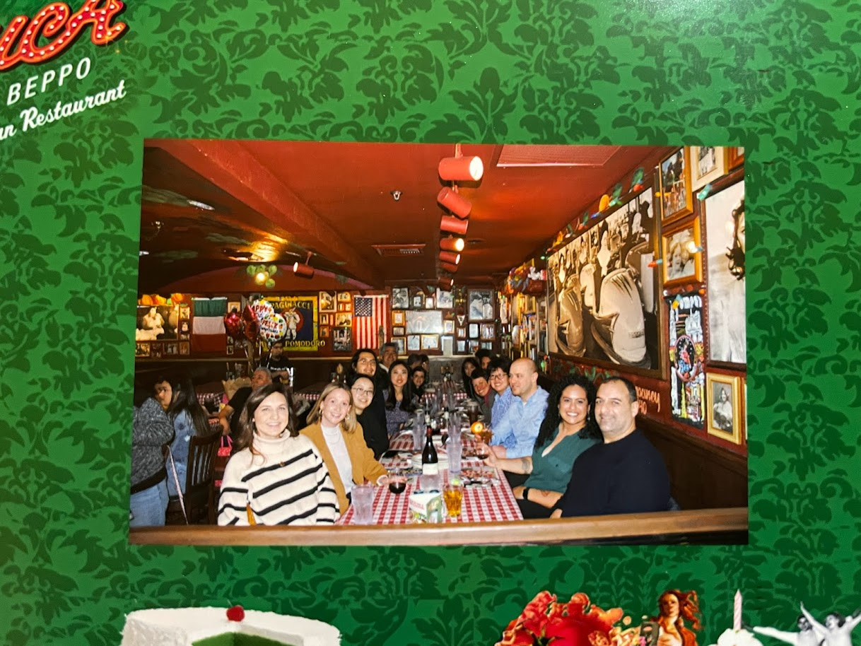 Picture of a polaroid photograph of 2 rows of people in a restaurant placed on a wall.