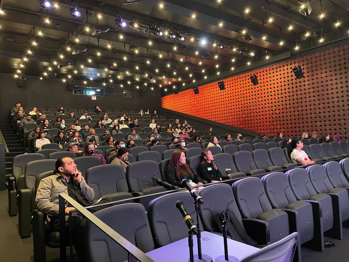 A room of people sitting down in rows of chairs and looking out of frame.