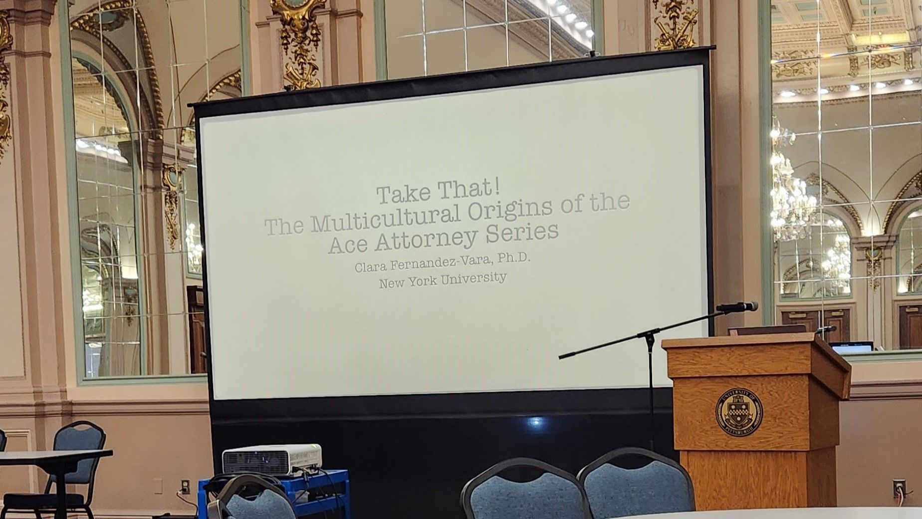 A projector screen with the words "Take That! The Multicultural Origins of the Ace Attorney Series"