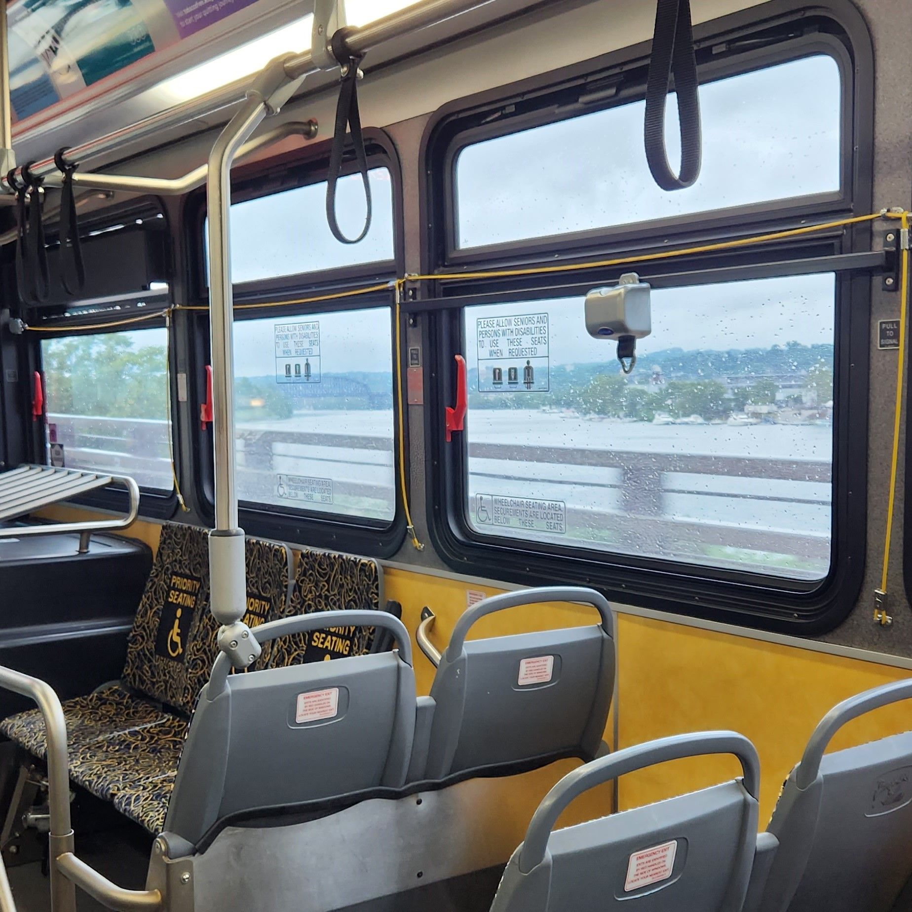 Bus seats and hanging straps next to windows overlooking a river outside.